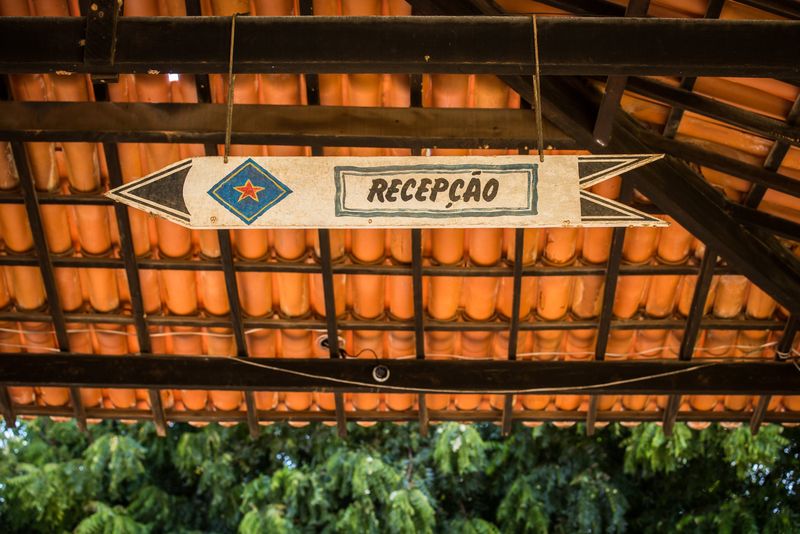 Placa pintada à mão indicando a recepção, sob o telhado de madeira e cerâmica