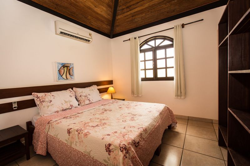 Quarto do bangalô com cama de casal, colcha florida, ar-condicionado e teto de madeira